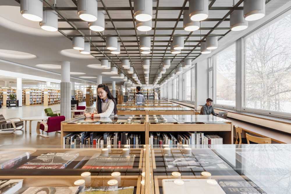 Biblioteca de espacio abierto con ventanales laterales y mesas de madera